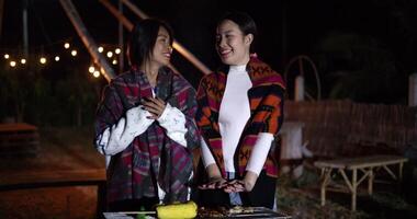 Two Asian women dress in warm clothing talk and share a happy moment together while grilling food and enjoying the cold night. video