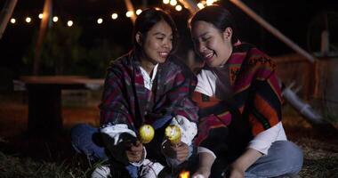 Handheld selective focus shot,Two Asian siblings enjoy talking and grilling corn while sitting around a warm campfire on a chilly evening. video