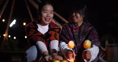 Handheld selective focus shot, Two Asian siblings enjoy talking and grilling corn while sitting around a warm campfire. video