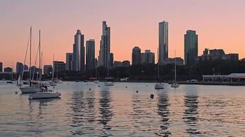 Chicago Skyline at Sunset, A breathtaking view of the Chicago skyline with towering skyscrapers reflecting on the calm waters of the harbor, as sailboats float peacefully under a pastel-colored sky. video