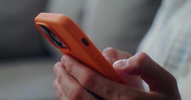 Close-up of a mobile phone with three cameras, in an orange case in men's hands. Man typing on smartphone, no face video