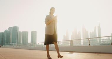 A woman in business clothes walks around the city on a bright sunny day and uses the phone video