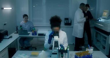 Work in a medical laboratory. A man and a woman approach with a question, showing the tablet to their colleague working with a microscope video