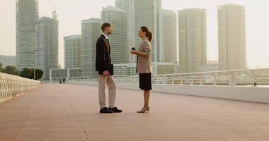 A man with a folder of documents and a woman with a disposable glass, dressed in business clothes, talking standing on the embankment of a modern metropolis video