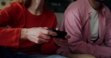 A man and a woman are laughing while playing games sitting on the couch at home and using joysticks. The moves from a woman's hands to her face video