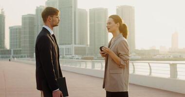 A man in glasses with a folder of documents in his hands and a woman with a disposable glass, dressed in business clothes, talking with a serious look standing on the embankment video