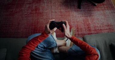 A woman in casual clothes playing games with a joystick, sitting on a sofa in a lotus position, top view, no face, close-up of female hands video
