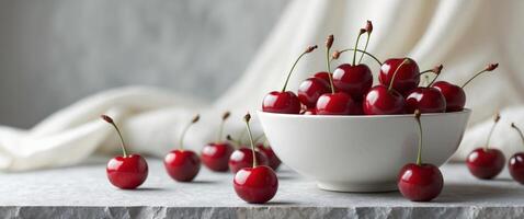Fresh Red Cherries in White Bowl on Gray Surface with Soft Light and Textile Background photo
