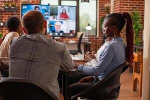 Employees brainstorm strategy ideas in virtual meeting, collaborating with remote team on digital monitor. Office workers and clients connect remotely through call, reviewing business project. photo