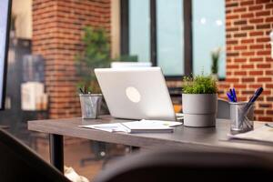 Vacant brick wall room with well organized desk containing office stationery, paperwork and open laptop, ready for use. Modern workspace with nobody, prepared for business researching and planning. photo
