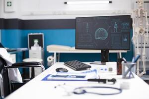 Empty clinic room with computer screen displaying brain and body scans, focused on neurology and computed tomography. Doctors desk with medical files and modern equipment is ready for health analysis. photo