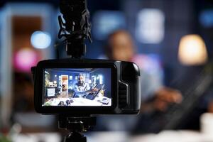 Focus on professional production camera used for capturing footage of BIPOC content creator in blurry background filming tech reviews for his internet channel, showcasing gaming keyboard photo