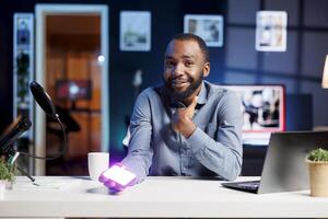 Tech engineer filming technology review of mini RGB lights device illuminating in different colors for online channel. Cheerful influencer presenting helpful production tool to subscribers photo