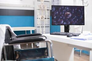 Digital display of virus cells in vacant doctors office focuses on healthcare response to illness. Desktop pc with microscopic germs on display, is on wheelchair accessible desk ready for research. photo