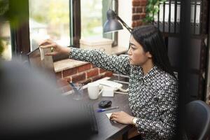 Professional woman adding post it reminders to computer screen, analyzing business analytics and preparing for upcoming deadlines at office desk. Female employee tracks her tasks with adhesive note. photo