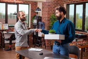 Male coworkers fist bumping in brick wall office, greeting each other, ready to work at startup company. Friendly interaction between businessmen in modern workspace, symbolizing teamwork and success. photo
