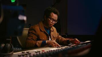 Music producer using audio mixer in professional studio, adjusting volume levels while pressing buttons and sliders on control desk. Sound designer works with digital audio software. Camera A. photo