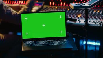 Music production engineer mixing and mastering music in control room, using laptop with greenscreen display. Skilled audio technician working with recording software on pc, pushing faders. Camera A. photo
