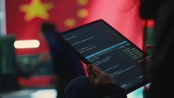 Chinese hacker uses a tablet in governmental cyber operations office to work on hybrid warfare and political manipulation. Inflicting manipulation and propaganda for the communism ideology. Camera A. photo