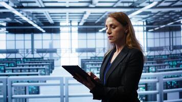 Computer scientist doing checkup, inputting data on tablet of needed fixes in server hub. Woman working in data center housing advanced data storage infrastructure supporting IT workloads, camera B photo