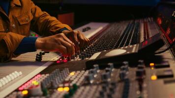African american producer uses control desk with automatic equalizer, mixer and sliders to edit tracks in post production. Sound engineer processing audio recordings, mixing console. Camera B. photo