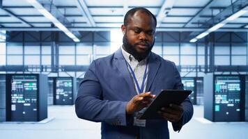 Software developer managing data center with advanced technology, ensuring efficient network management. Admin walking in server room, optimizing data center infrastructure with tablet, camera B photo