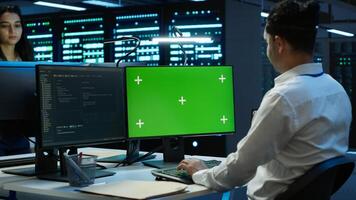 Programmer overseeing data center using isolated screen computer, ensuring system can handle networking tasks. IT expert in server room tracking network traffic with chroma key PC, camera A photo