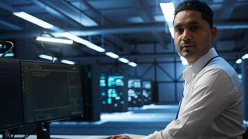 Portrait of smiling technician in data center implementing and managing infrastructure to ensure optimal performance and reliability. Happy IT specialist in server room coding on computer, camera B photo