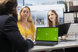 Financial advisor showing data graphs on green screen notebook to customers, analyzing market trends to do forecasting. Clients checking investment plan on chroma key laptop photo