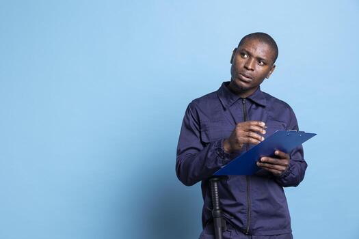 Security officer creating a list on clipboard files against blue background, keeping evidence of things while he is on duty. Bodyguard thinking of details to write down on papers. photo