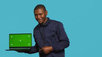 Radiant security guard working protection job presenting mockup laptop. Portrait of joyous bodyguard showcasing isolated screen notebook, isolated over studio background, camera A photo