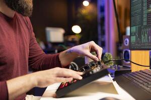 Composer artist twisting pre amp knobs and adjusting volume levels in home studio, mixing and mastering tunes for post production. Young singer recording and editing soundtracks. photo