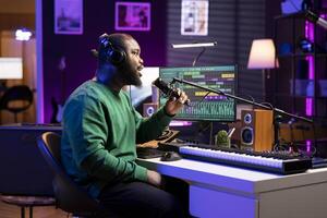 Artist composer recording a new track on his home studio microphone, editing his song with professional gear. Adjusting volume levels and adding sound effects, mix and master. photo