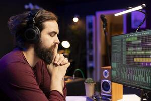 Music producer listening carefully his audio recording after editing and adjusting volume levels in home studio. Artist using daw software interface to enhance acoustics, stereo gear. photo