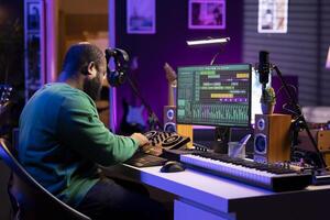 Skilled male composer producing new songs on his mixing console, operating on professional gear in home studio. Artist audio engineer twisting knobs to adjust sound levels on tracks. photo