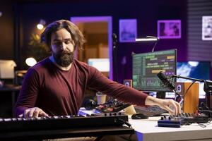 Audio engineer mixing and mastering soundtracks in home studio, adding piano electronic keyboard tunes. Young professional composer creating music with stereo equipment and amplifier. photo