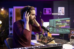 Skilled confident musician editing tunes with daw software on microphone to create tracks with mixing console. Talented songwriter producing music and composing on stereo gear. photo