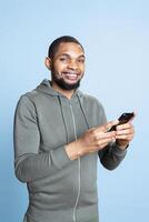 African american confident man browsing online websites and using social media, answering his texts and smiling on camera. Lively relaxed person standing against blue background. photo