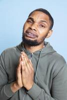 Young sorrowful person begging for something in studio, holding hands in a prayer and beseeching to receive mercy. Appealing in misery and having belief, pleading for forgiveness. photo