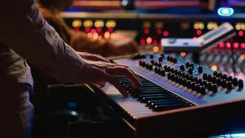 Skilled artist playing piano electronic keyboard in control room, recording new tracks with midi controller and mixing console. Young musician practicing on synthesizer in record studio. Camera A. photo