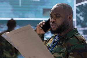Army intelligence specialist transmitting real time data on phone call, studying surveillance footage via satellite to enhance national security and process information. Military control room. photo