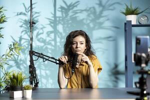 Streamer recording live broadcast in studio, using smartphone on tripod and mic to ensure crisp sound and quality. Internet star speaks into professional microphone, talking with followers photo