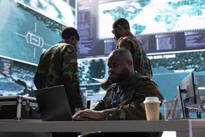 Army staff in a command post base oversees intelligence gathering activity for reconnaissance mission, live surveillance for security protocols. Military personnel helps in a defense operation. photo