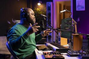 Young singer recording his new composed song on microphone, editing the tracks with mixing console and professional software. Artist manipulating sounds to create a good soundtrack. photo