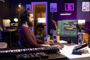 Musical producer working on editing audio recordings with daw software interface on pc, adjusting volume levels for new songs. Artist adding sound effects on tunes, music industry concept. photo