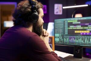 Music engineer listening his audio recording on headset after editing and adding new sound effects in home studio. Producer using daw software interface on pc to enhance music volume, stereo tool. photo