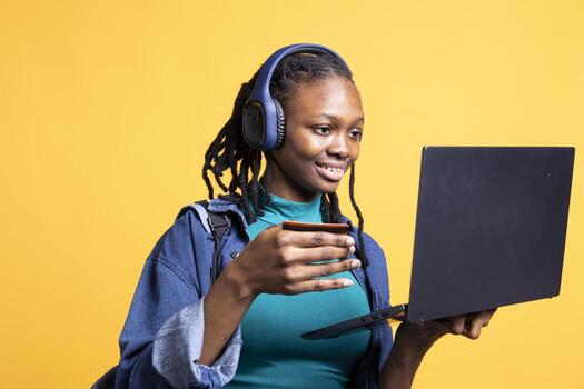 Joyful woman listening music adding payment method on website using laptop, enjoying sales period, studio background. Girl doing financial transactions on internet using credit card on notebook photo