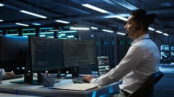 Data center computer scientist wearing mic headset, doing installation of networking equipment. Server hub IT professional talking in microphone with system administrators, camera B photo