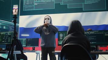 Anonymous person with mask asks for ransom in Russian governmental hacking room with the national flag. Dealing with cyber espionage, disinformation campaigns and hybrid war propaganda. Camera B. photo