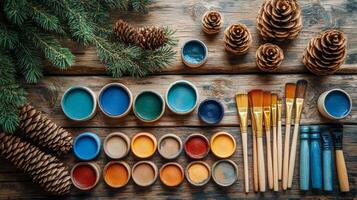 Paint brushes, paint and pine cones on a wooden table photo